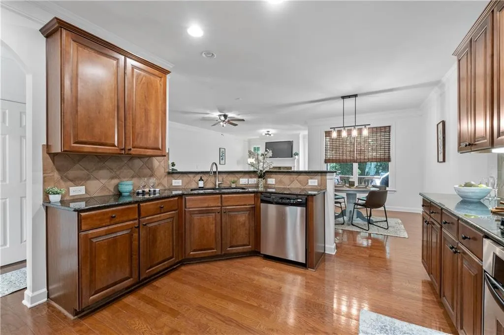 Kitchen with a peninsula, brown cabinetry, stainless steel dishwasher, crown molding, and light wood-style flooring