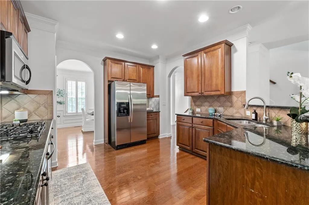 Kitchen featuring arched walkways, decorative backsplash, appliances with stainless steel finishes, light wood-style flooring, and brown cabinetry