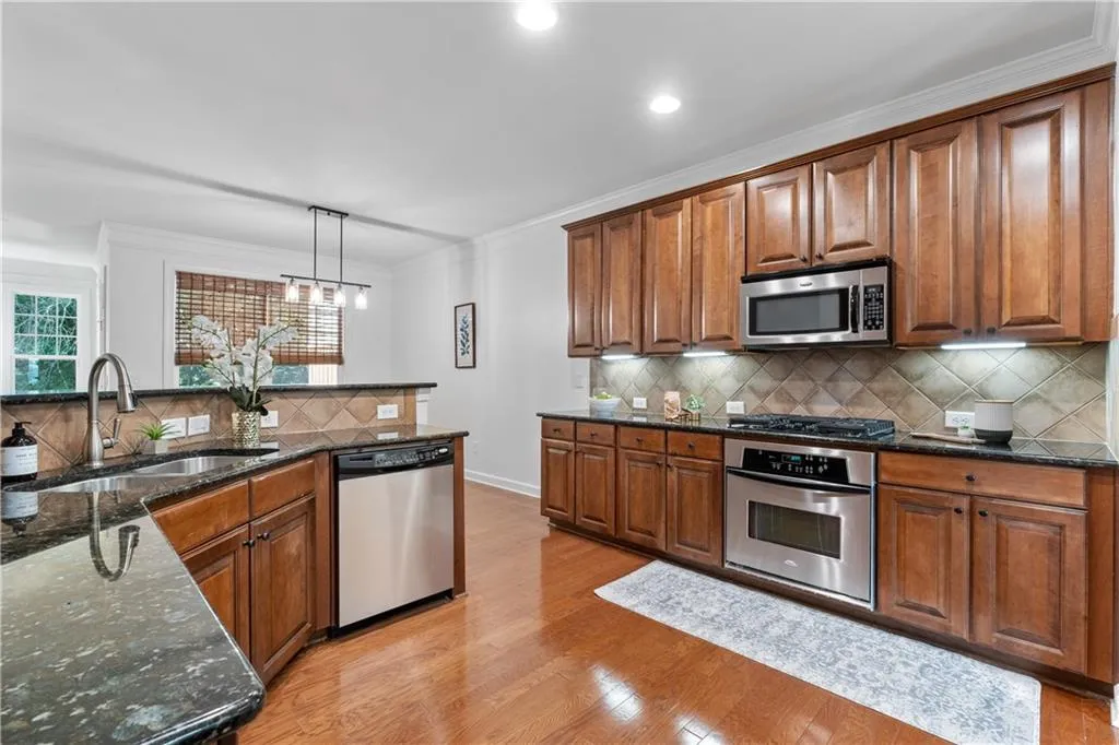 Kitchen featuring crown molding, appliances with stainless steel finishes, light wood-style floors, decorative backsplash, and brown cabinetry