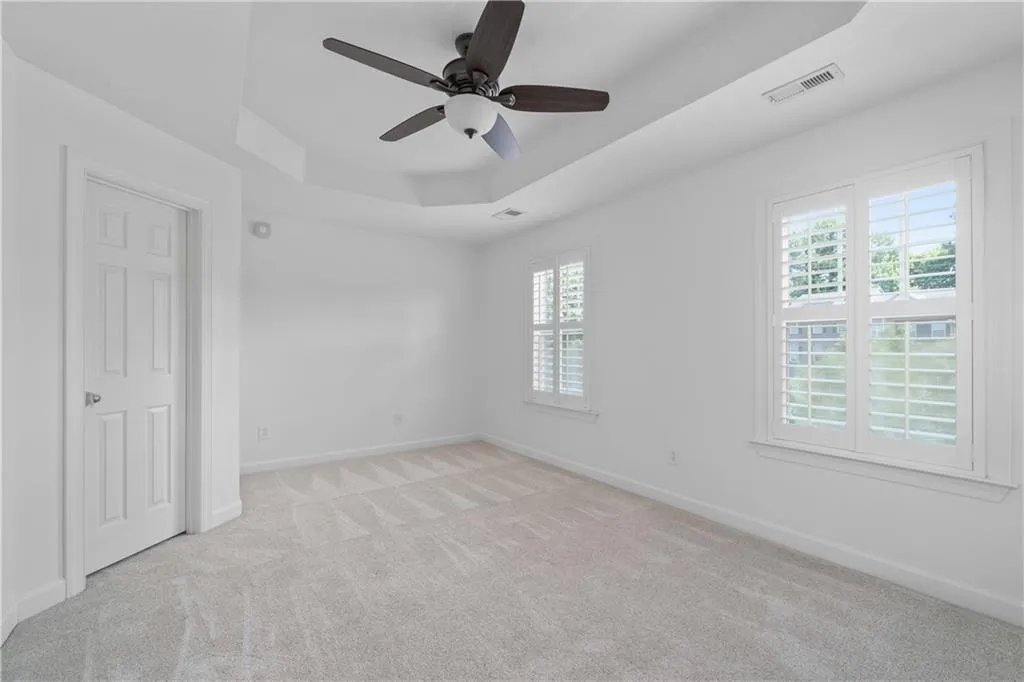 Carpeted empty room featuring a raised ceiling and ceiling fan