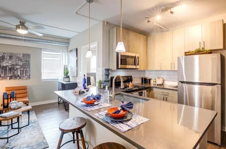 Kitchen with stainless steel appliances, light wood finish cabinetry, a peninsula, backsplash, and a kitchen breakfast bar