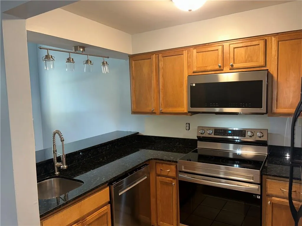 Kitchen featuring appliances with stainless steel finishes, a sink, brown cabinets, and dark stone counters