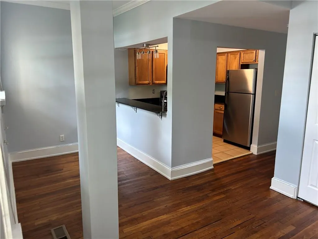 Kitchen with freestanding refrigerator, dark countertops, ornamental molding, brown cabinetry, and hardwood / wood-style flooring