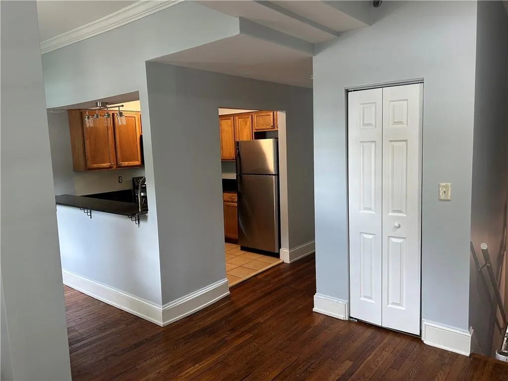 Kitchen featuring freestanding refrigerator, dark countertops, ornamental molding, brown cabinetry, and wood finished floors