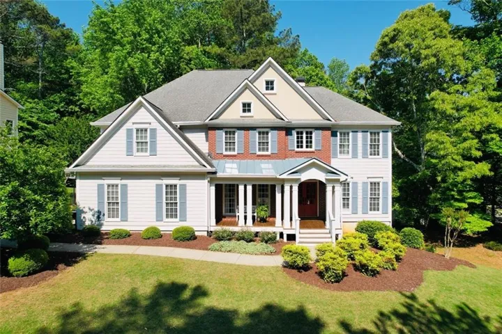 Two-story residence featuring light siding, red brick accents, and a prominent front porch with white columns