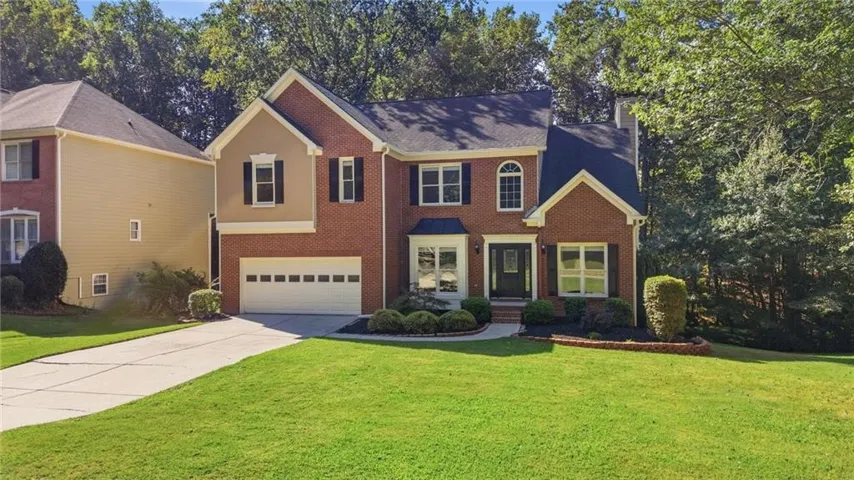 Brick and siding exterior with a two-car garage, mature landscaping, and a manicured lawn