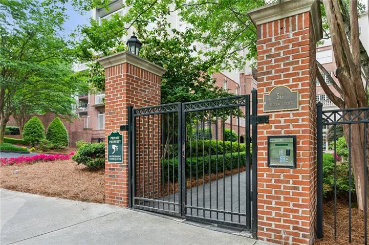 Brick pillars with stone caps, decorative wrought iron gate, integrated call box, and mature landscaping