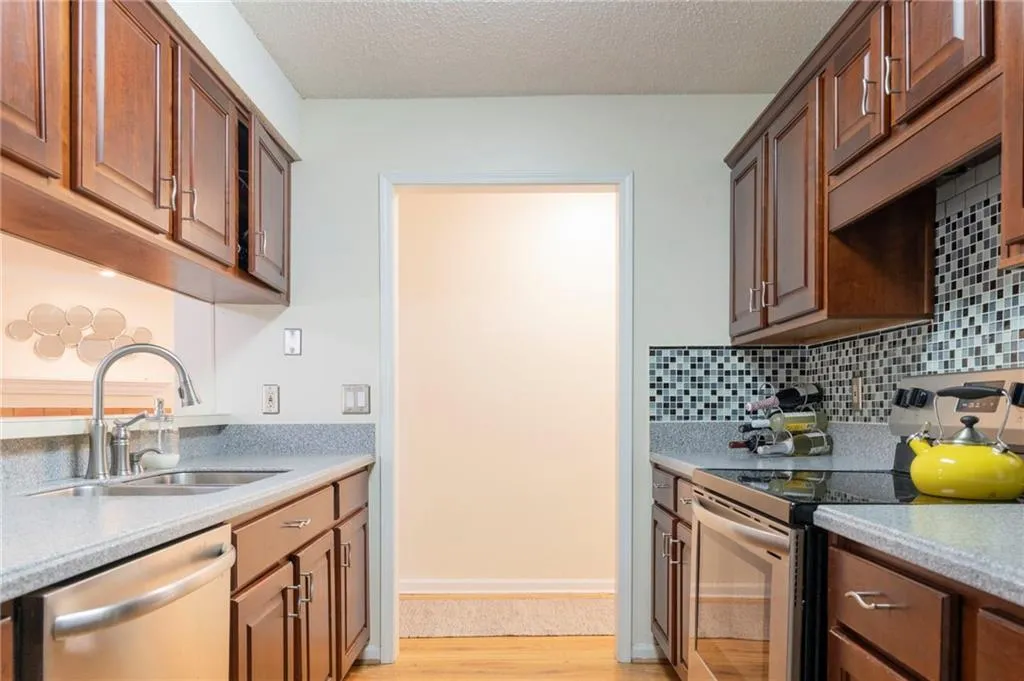 Kitchen with electric stove, tasteful backsplash, sink, dishwasher, and light hardwood / wood-style floors