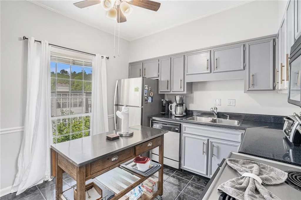 Kitchen with ornamental molding, stainless steel appliances, dark countertops, gray cabinetry, and a ceiling fan
