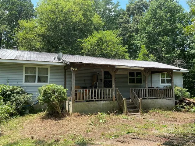 Property exterior featuring a full-width covered porch with wood railing and columns, vinyl siding, and a metal roof