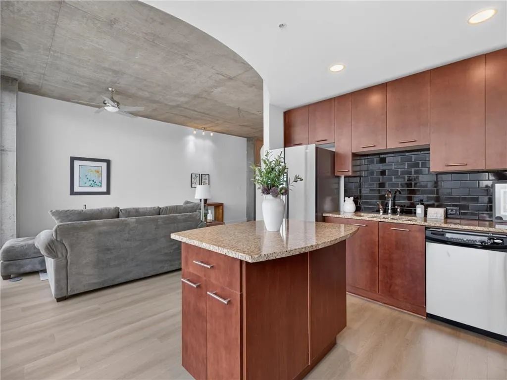 Kitchen island with stone countertop, wood-finish cabinetry, stainless steel appliances, and dark tile backsplash