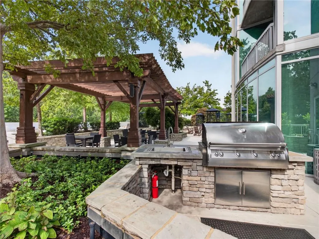 Outdoor kitchen featuring a built-in stainless-steel grill and sink adjacent to the pool, outdoor spa, and fire pit