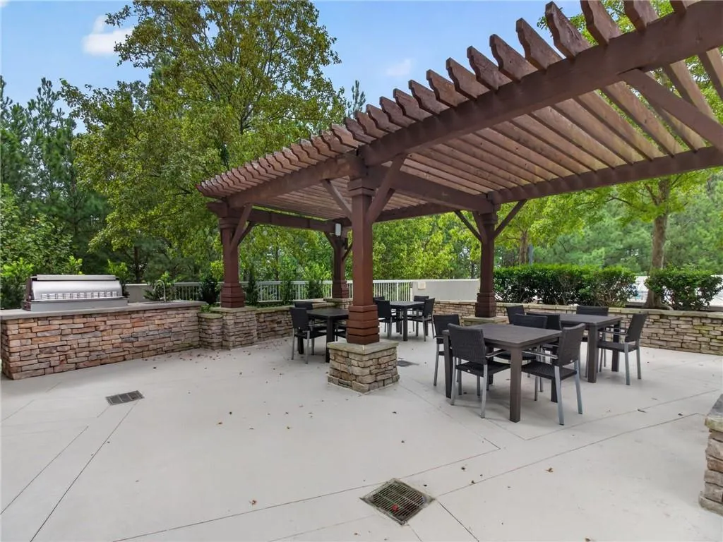 Wood pergola structure over paved patio with stone-faced built-in grill station adjacent to the pool, outdoor spa, and fire pit area.