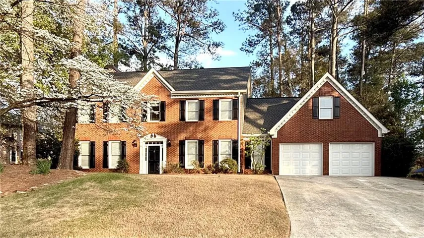 Colonial inspired home with a front lawn, driveway, brick siding, and a shingled roof
