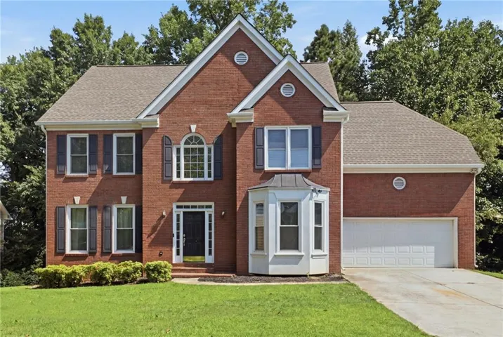 Brick exterior with white trim, arched window, bay window, two-car garage, and manicured lawn