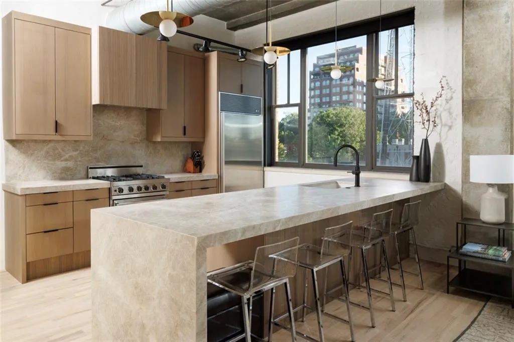 Full-height windows, a waterfall island, wood-finish cabinetry, a stainless steel range, and stone countertops