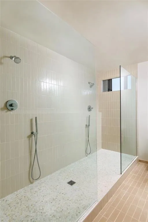 Expansive shower with glass enclosure, dual showerheads, dual handheld sprayers, and mosaic tile flooring