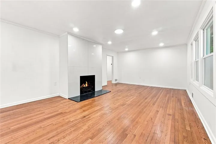 Hardwood flooring, recessed lighting, multiple windows, sleek fireplace with a black hearth, and white walls