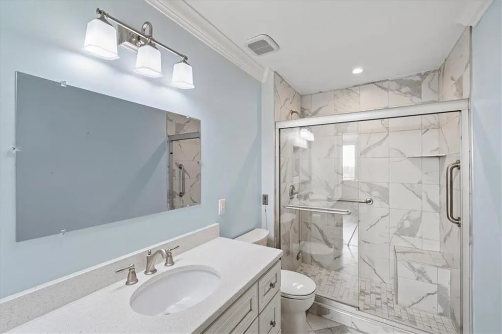 This renovated primary bathroom has beautiful solid surface countertops and a stunning shower stall complete with hand rails.