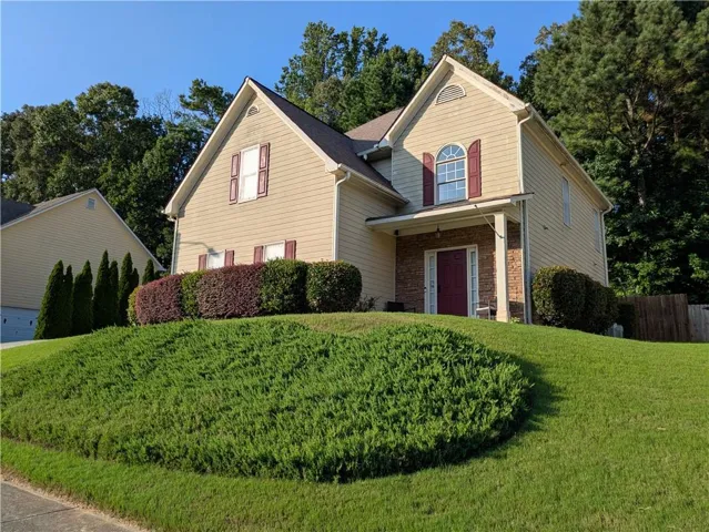 Two-story colonial with cream-colored vinyl siding and brick accents, featuring gabled rooflines, arched windows, and a burgundy front door