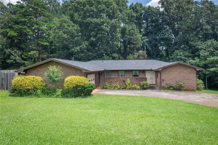 Brick exterior with a dark shingle roof, mature landscaping, an attached garage, and a lush green lawn