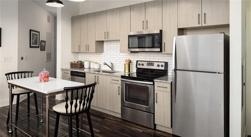 Kitchen featuring light stone counters, light brown cabinets, dark hardwood / wood-style flooring, and appliances with stainless steel finishes