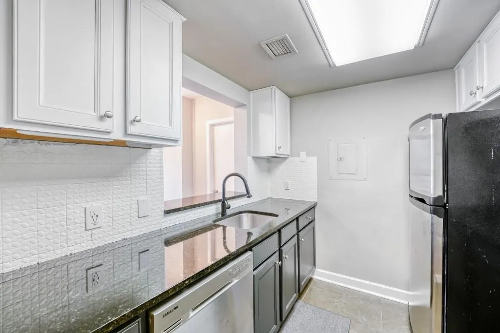 Kitchen with dark stone countertops, stainless steel appliances, backsplash, and white cabinetry