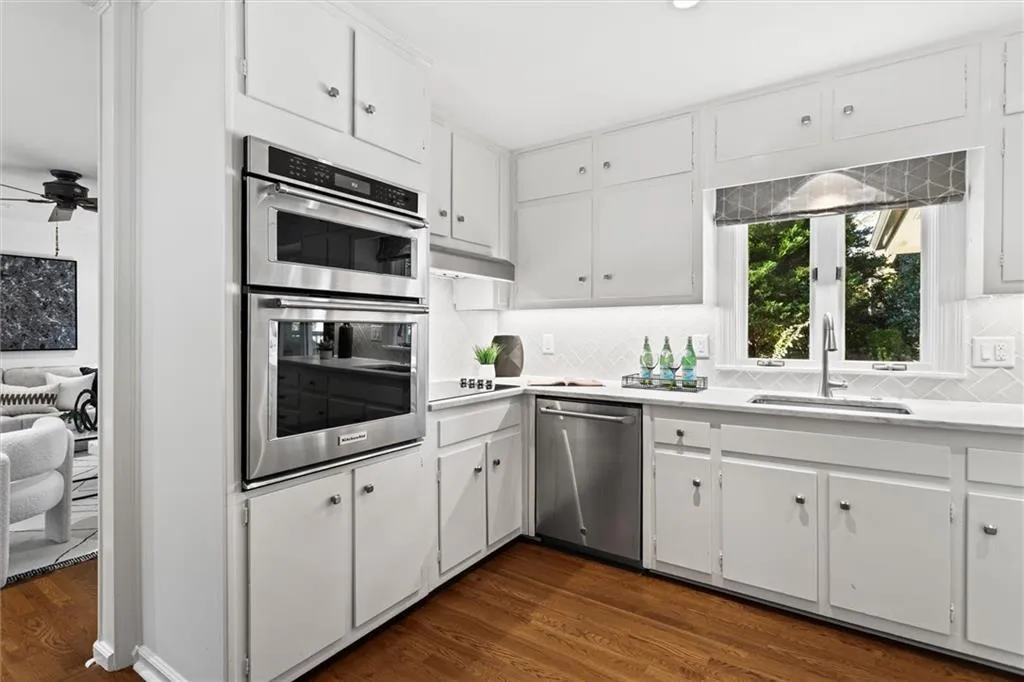 Kitchen featuring white cabinetry, stainless steel appliances, decorative backsplash, dark wood-style flooring, and ceiling fan