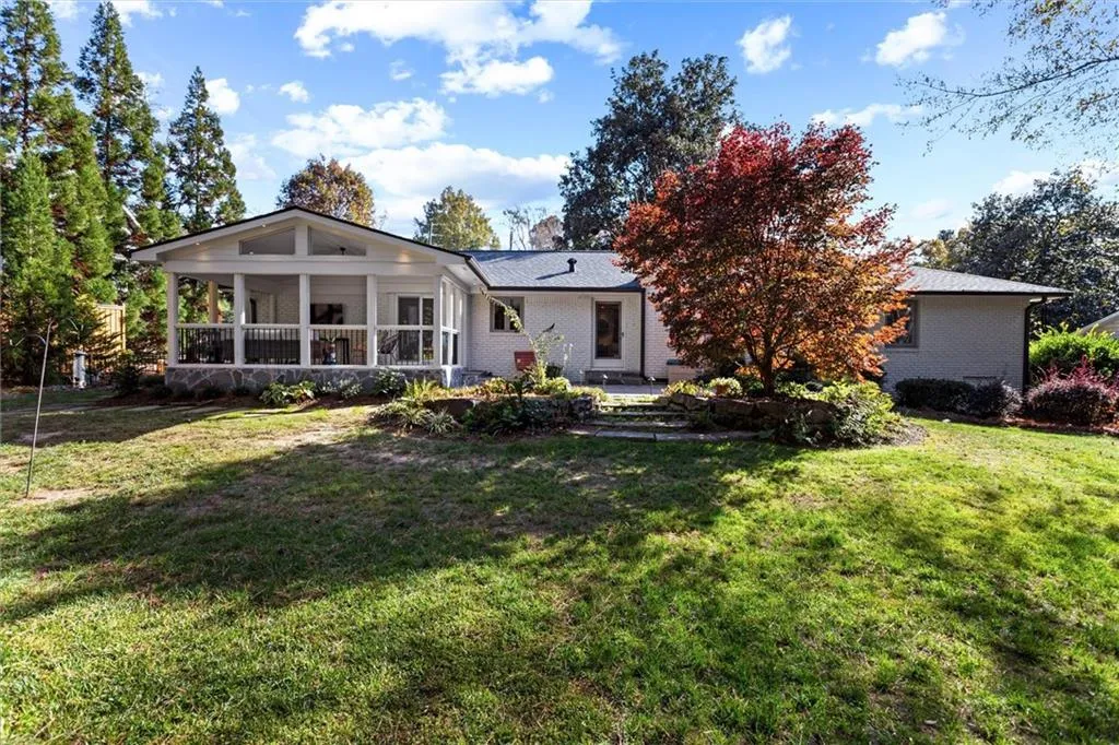 Back of house featuring a lawn, brick siding, a patio, and a sunroom