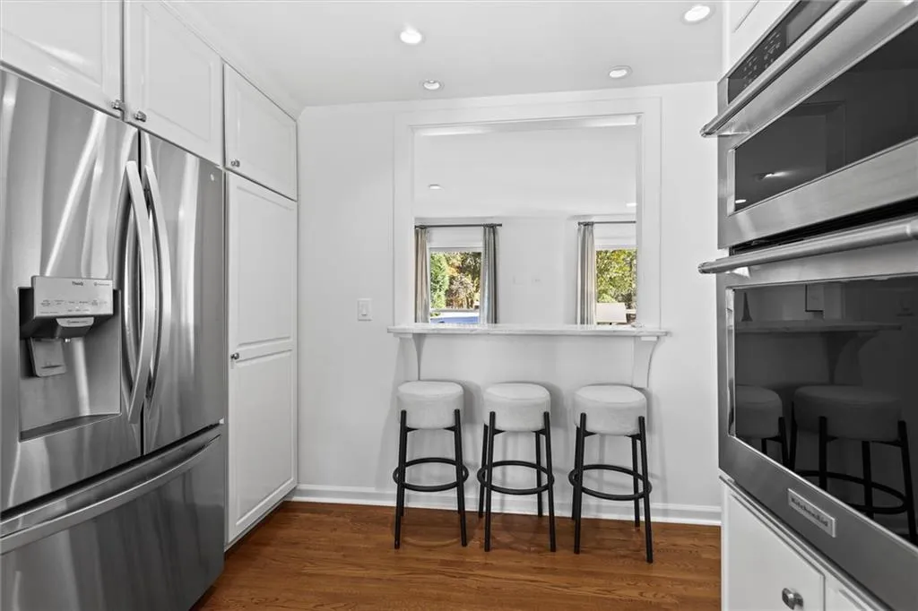 Kitchen featuring stainless steel appliances, white cabinetry, a breakfast bar, recessed lighting, and dark wood-style floors