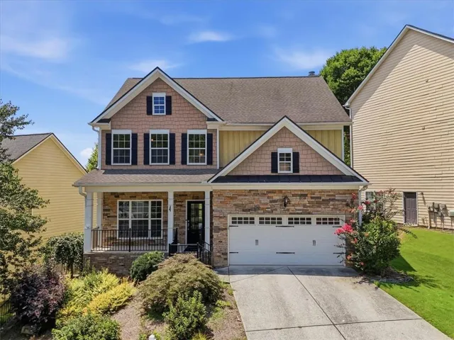 Two-story residence featuring a covered front porch, stone and siding exterior, two-car garage, and established landscaping