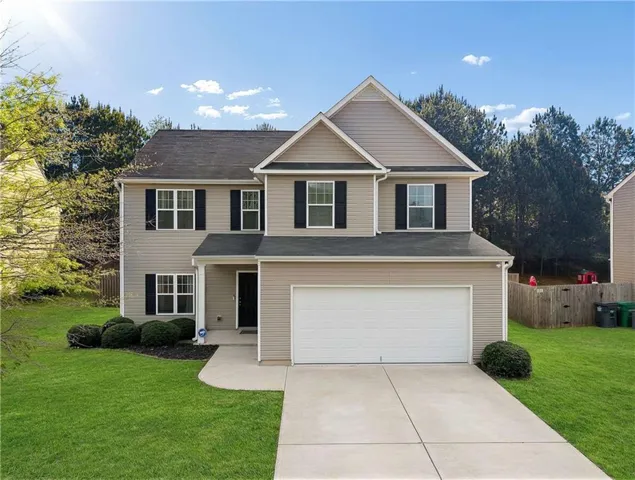 Two-story residence featuring light-colored siding, contrasting dark shutters, a two-car garage, and a concrete driveway