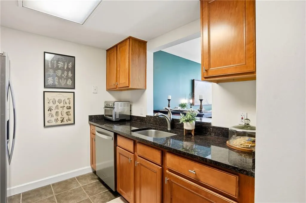 Kitchen featuring dark stone counters, light tile patterned floors, appliances with stainless steel finishes, and brown cabinets