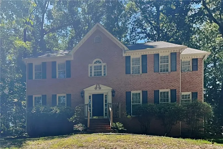 Brick facade colonial-style residence with dark shutters and a central arched window