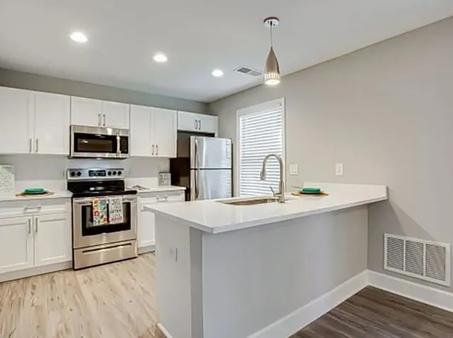 Kitchen featuring white cabinetry, appliances with stainless steel finishes, hanging light fixtures, and light hardwood / wood-style floors