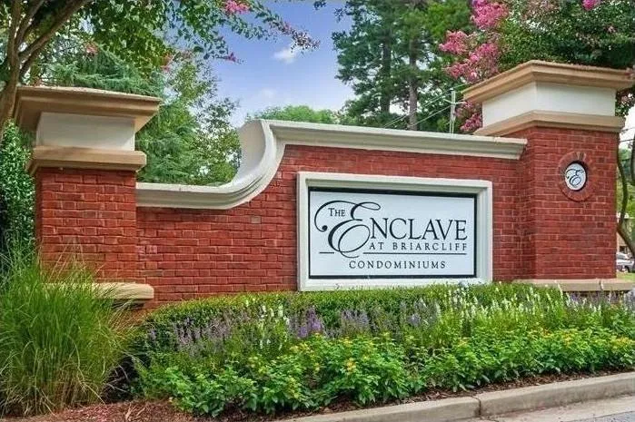 Brick-clad entrance monument featuring a white central sign panel, decorative pilasters with coping, integrated landscaping, and a red brick base