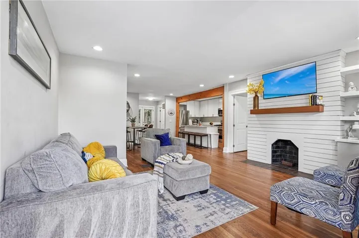 Wood-finish flooring, recessed lighting, and a white shiplap fireplace with a wood mantle