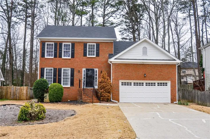 Brick two-story colonial-style residence featuring a two-car garage with a white panel door, black window shutters, and a dark asphalt shingle roof