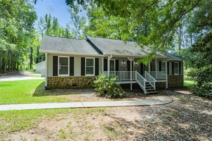 Front facade featuring stone veneer, vinyl siding, a covered porch with white railings, and a concrete walkway