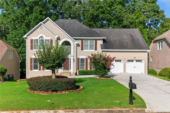 Colonial home featuring a front yard, concrete driveway, a garage, and stucco siding