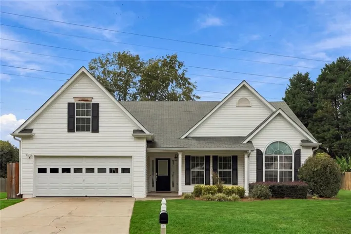 White siding exterior featuring a covered entry, an arched window, a two-car garage, and a manicured lawn