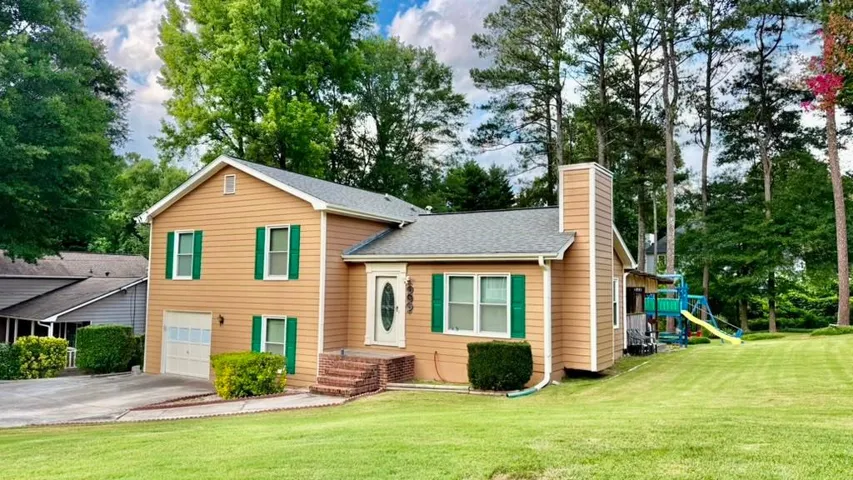 Split-level home featuring light brown siding, green window shutters, and a prominent brick chimney