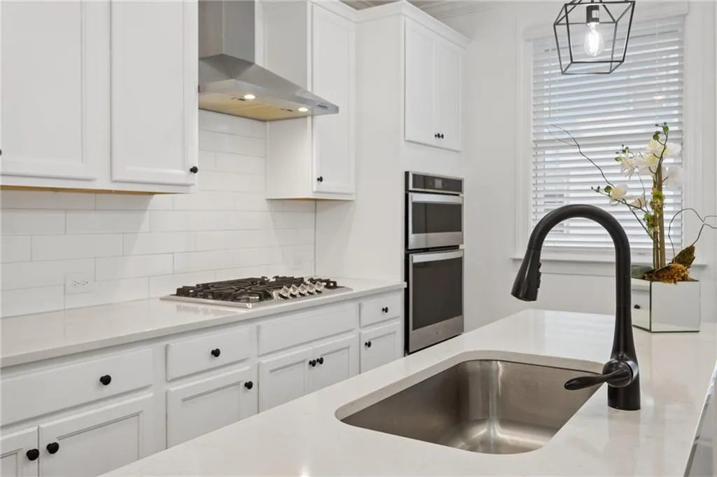 White shaker-style cabinets, stainless steel appliances, 5 burner gas cooktop, subway tile backsplash, and quartz countertops