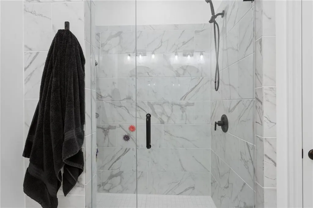 Glass-enclosed shower with white marble-like tile