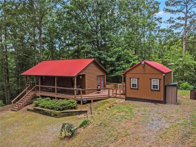 Log-sided main structure with a red metal roof and a spacious wrap-around deck