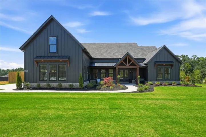 Modern farmhouse exterior featuring dark vertical siding, contrasting wood-beam entry, a gabled roofline, and established landscaping