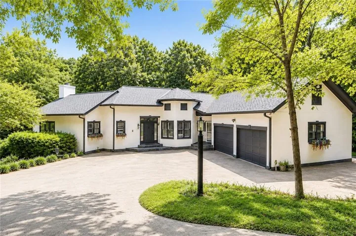 White stucco exterior with dark trim accents, a multi-car garage, and a curved drive