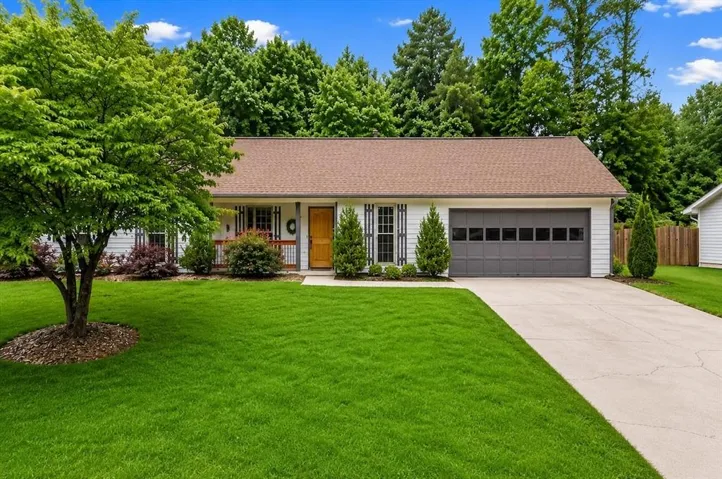 White siding exterior with a brown shingle roof, attached garage with a dark gray door, concrete driveway, and mature landscaping