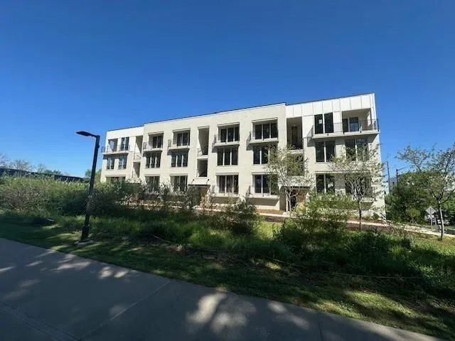 Contemporary building exterior with multiple balconies, large windows, and a paved walkway