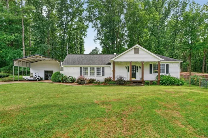 Ranch-style residence with a covered front porch, white siding, and a detached carport with an enclosed section
